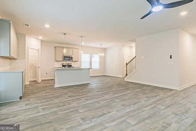 unfurnished living room with stairs, light wood finished floors, visible vents, and baseboards