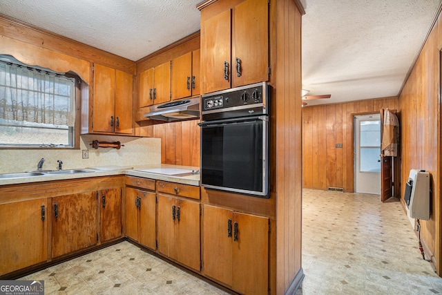 kitchen with sink, heating unit, wood walls, stovetop, and oven