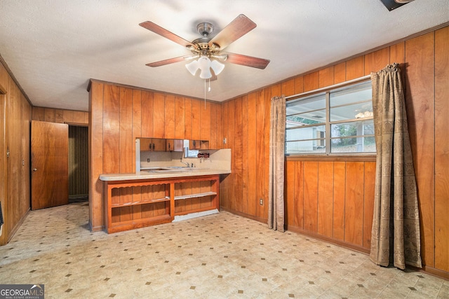 kitchen featuring kitchen peninsula, wood walls, ceiling fan, and a textured ceiling