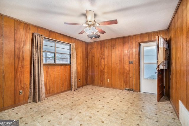 unfurnished room with a textured ceiling, ceiling fan, and wood walls