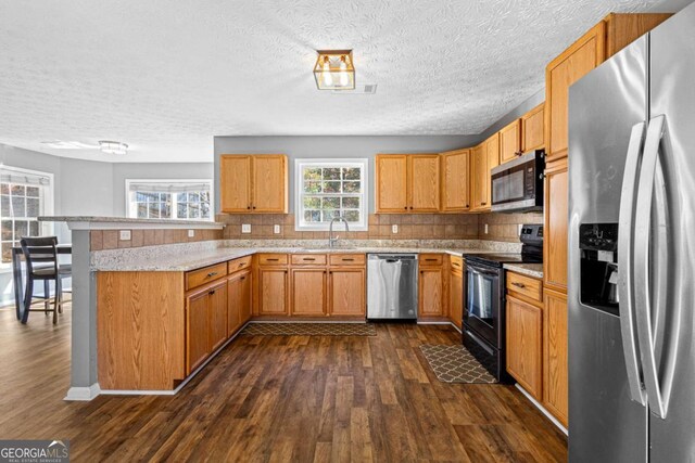 kitchen featuring kitchen peninsula, light stone countertops, dark hardwood / wood-style flooring, tasteful backsplash, and stainless steel appliances