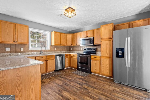 kitchen with sink, light stone counters, dark hardwood / wood-style flooring, decorative backsplash, and appliances with stainless steel finishes