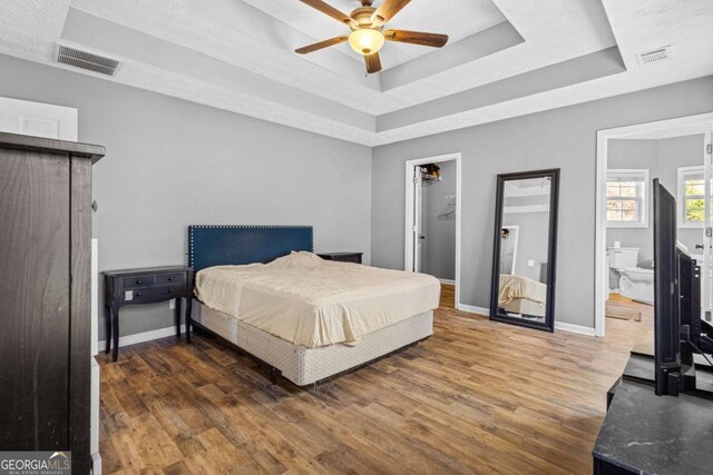 bedroom featuring dark wood-type flooring, a raised ceiling, a walk in closet, ceiling fan, and a closet