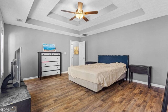 bedroom with a raised ceiling, ceiling fan, and dark hardwood / wood-style flooring