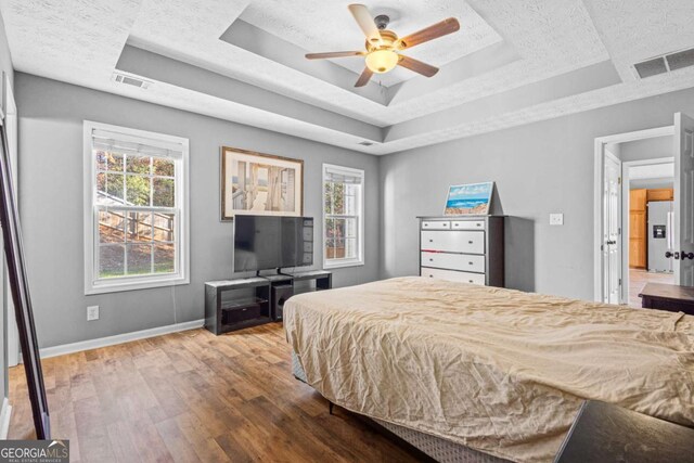 bedroom with ceiling fan, wood-type flooring, white refrigerator with ice dispenser, and a tray ceiling