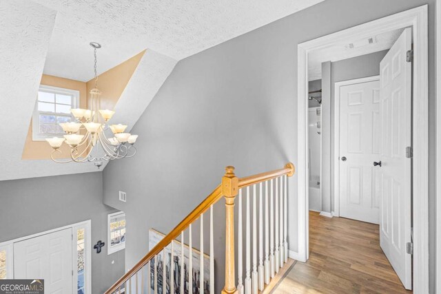 corridor with a textured ceiling, hardwood / wood-style floors, vaulted ceiling, and a notable chandelier