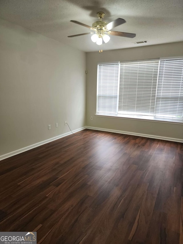 empty room with ceiling fan, dark wood-type flooring, and a textured ceiling