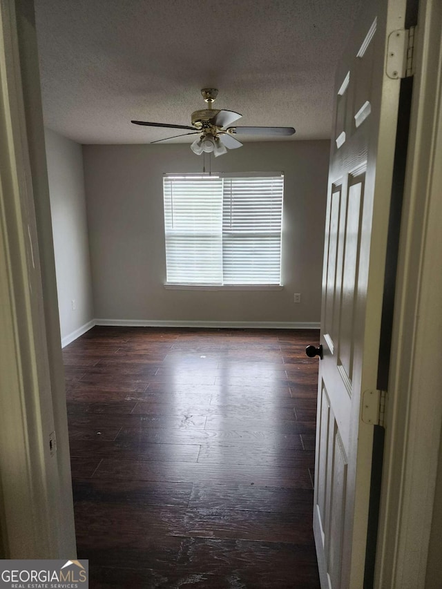 empty room with ceiling fan, dark wood-type flooring, and a textured ceiling