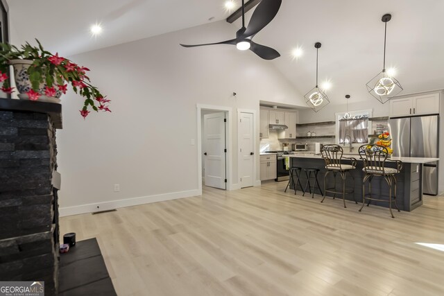 kitchen featuring stainless steel refrigerator, an island with sink, pendant lighting, white cabinets, and ceiling fan with notable chandelier