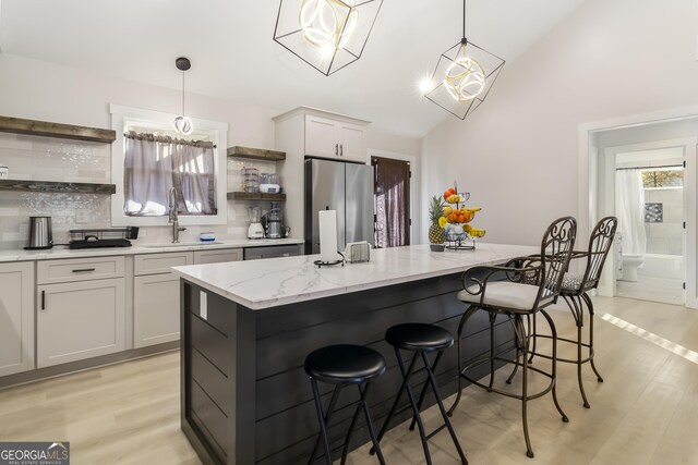 kitchen featuring stainless steel fridge, gray cabinets, decorative light fixtures, and a center island with sink