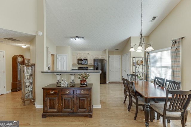 dining area with a notable chandelier, light wood-type flooring, a textured ceiling, and lofted ceiling