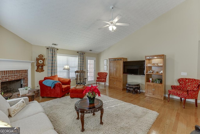 living room featuring lofted ceiling, ceiling fan, a textured ceiling, a fireplace, and light hardwood / wood-style floors