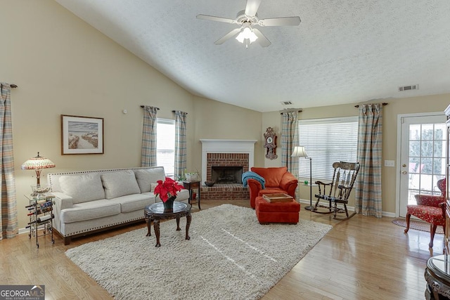 living room featuring a textured ceiling, a brick fireplace, vaulted ceiling, and light wood-type flooring