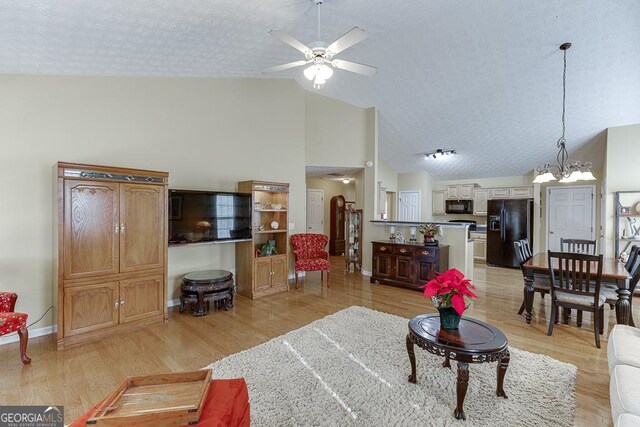 living room with a textured ceiling, ceiling fan with notable chandelier, light hardwood / wood-style floors, and high vaulted ceiling