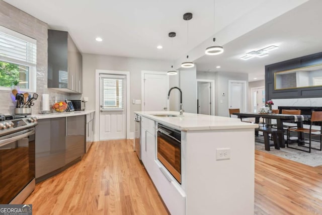 kitchen featuring a center island with sink, sink, hanging light fixtures, light wood-type flooring, and stainless steel appliances