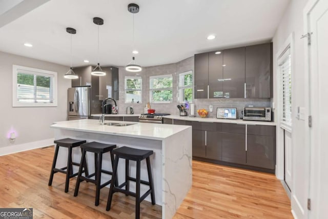 kitchen with backsplash, stainless steel appliances, sink, pendant lighting, and light hardwood / wood-style floors