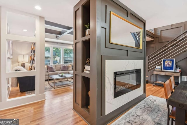 living room featuring a high end fireplace, light wood-type flooring, and beamed ceiling