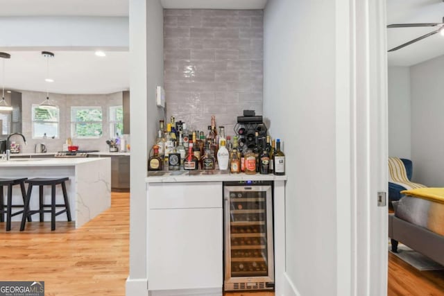 bar featuring decorative backsplash, hanging light fixtures, beverage cooler, and light wood-type flooring