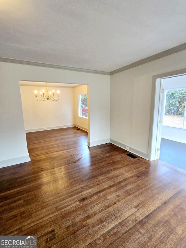 empty room featuring ornamental molding, dark hardwood / wood-style floors, and a notable chandelier