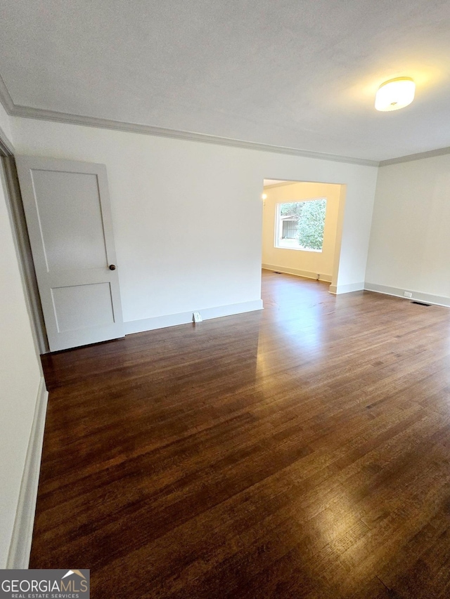 empty room featuring a textured ceiling, dark hardwood / wood-style floors, and ornamental molding