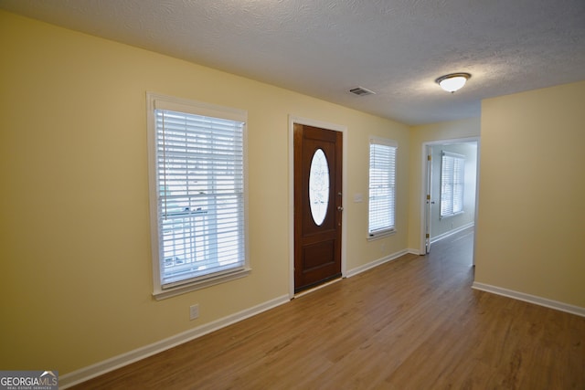 foyer entrance with wood finished floors, a textured ceiling, baseboards, and visible vents
