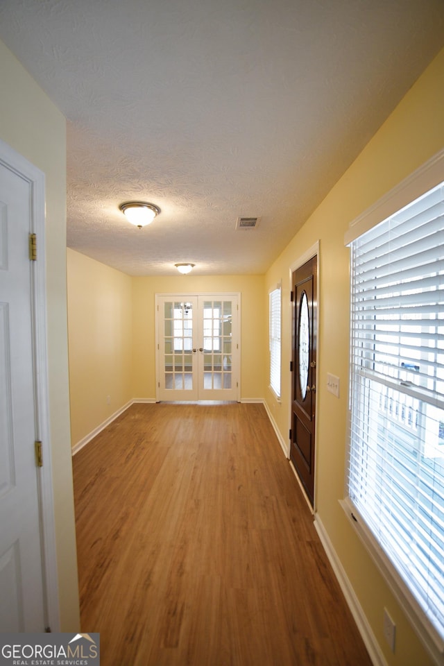 foyer entrance with a textured ceiling, visible vents, baseboards, wood finished floors, and french doors