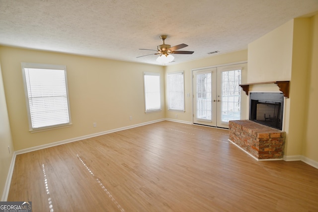 unfurnished living room featuring light wood-type flooring, a fireplace with raised hearth, a textured ceiling, ceiling fan, and visible vents