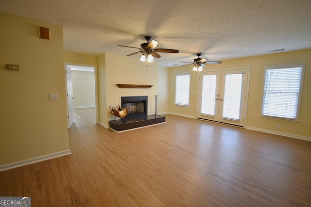unfurnished living room with a fireplace with raised hearth, a textured ceiling, ceiling fan, visible vents, and wood finished floors