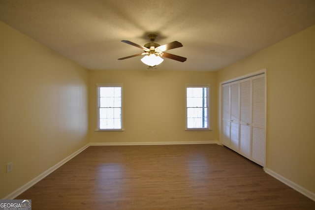 unfurnished bedroom with a ceiling fan, dark wood-type flooring, a closet, and baseboards