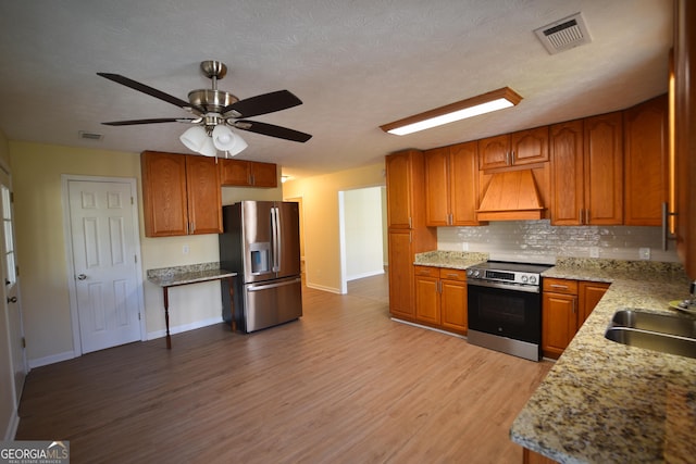 kitchen featuring tasteful backsplash, sink, stainless steel appliances, custom range hood, and light wood-type flooring