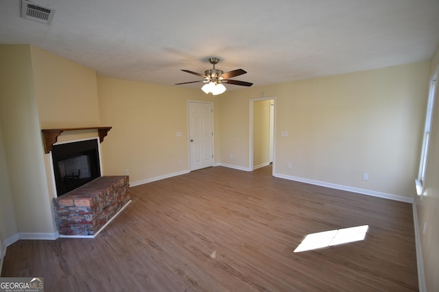 unfurnished living room with a fireplace, wood finished floors, baseboards, visible vents, and ceiling fan