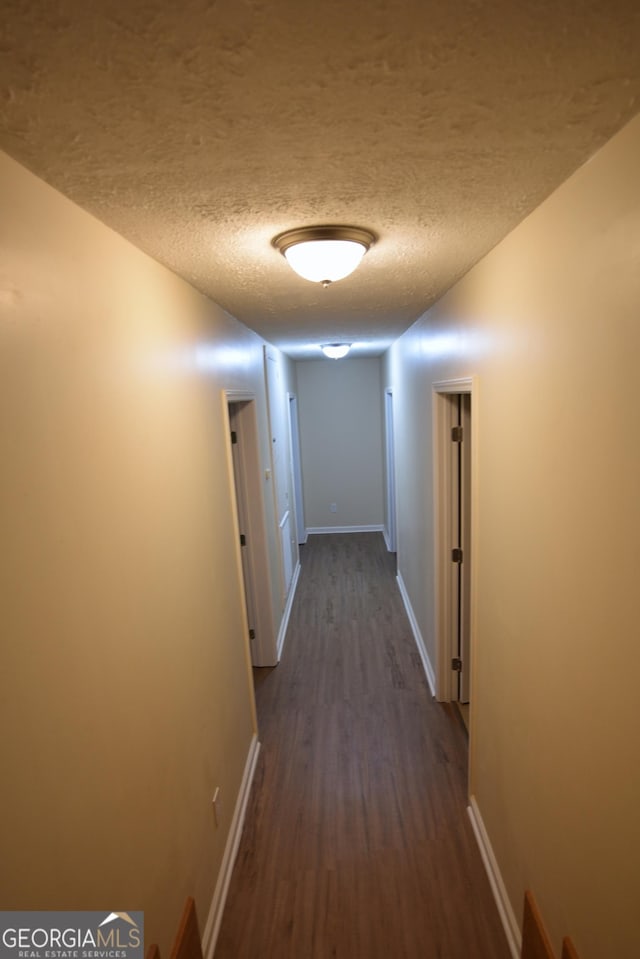 corridor with baseboards, dark wood-type flooring, and a textured ceiling