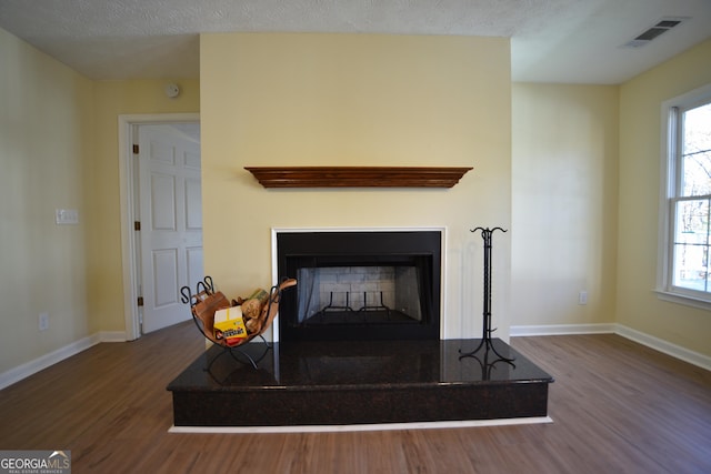 interior details featuring wood finished floors, a fireplace with raised hearth, a textured ceiling, baseboards, and visible vents
