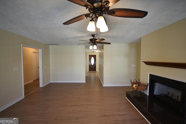 unfurnished living room with a textured ceiling, baseboards, wood finished floors, a ceiling fan, and a glass covered fireplace