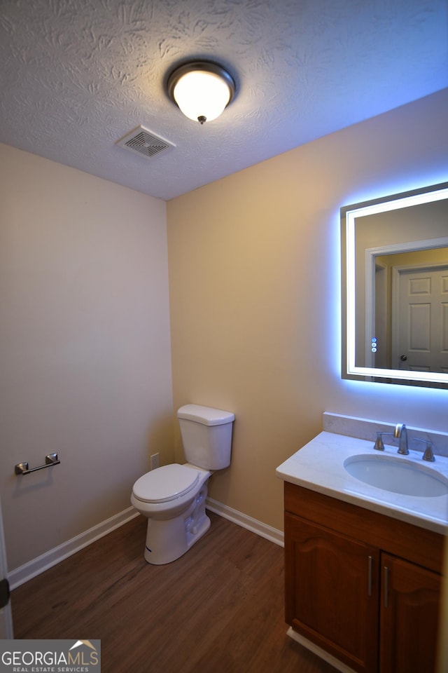 half bathroom featuring vanity, wood finished floors, a textured ceiling, baseboards, and visible vents