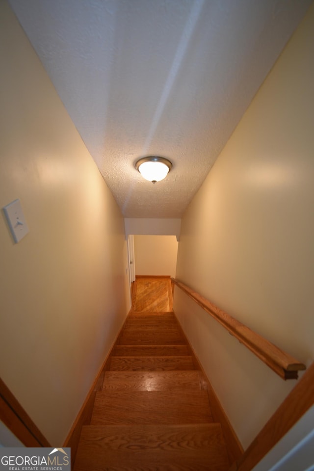 staircase featuring baseboards, wood finished floors, and a textured ceiling