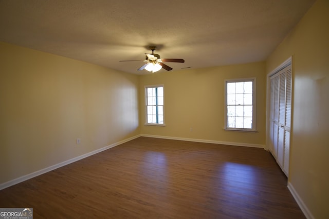 spare room with a ceiling fan, a textured ceiling, baseboards, and dark wood finished floors