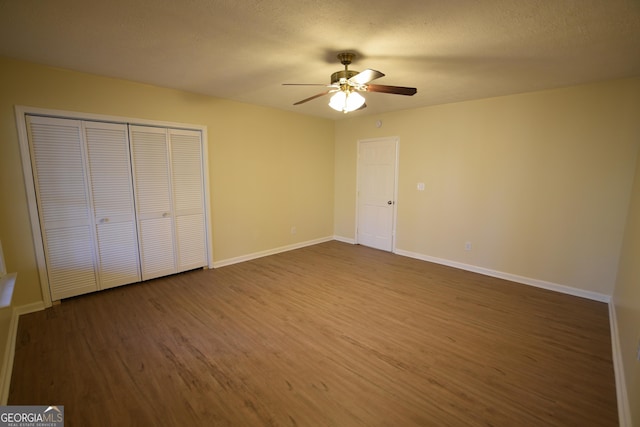 unfurnished bedroom featuring a closet, a textured ceiling, baseboards, a ceiling fan, and dark wood-style floors