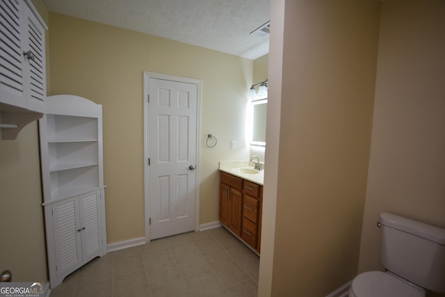 bathroom featuring toilet, vanity, a textured ceiling, baseboards, and visible vents