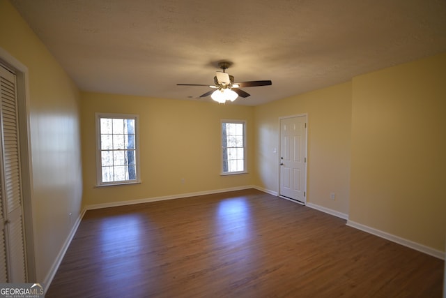 spare room featuring a healthy amount of sunlight, baseboards, dark wood-type flooring, and a ceiling fan