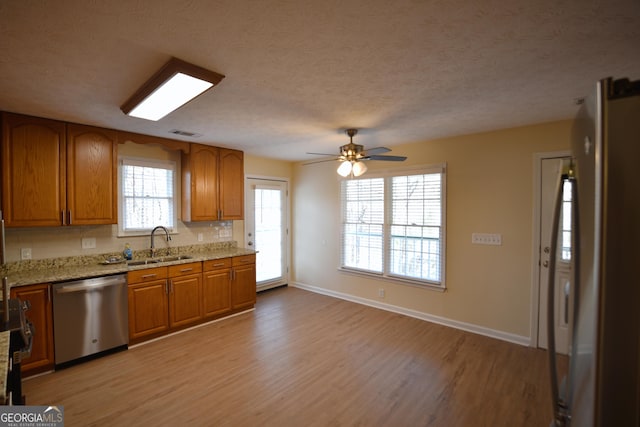 kitchen featuring light wood finished floors, a sink, brown cabinets, and dishwasher