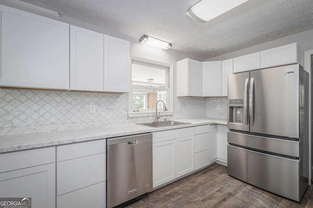 kitchen with appliances with stainless steel finishes, a textured ceiling, dark wood-type flooring, sink, and white cabinetry