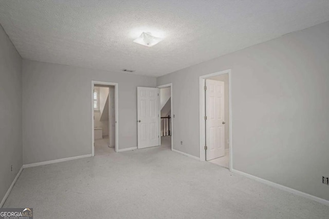 unfurnished bedroom with a textured ceiling, light colored carpet, and ensuite bath