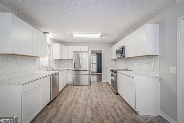 kitchen featuring appliances with stainless steel finishes, a textured ceiling, sink, light hardwood / wood-style floors, and white cabinetry