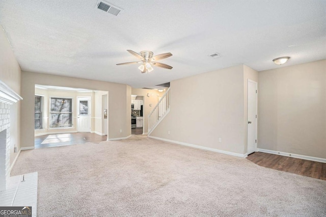 unfurnished living room with ceiling fan, carpet floors, a textured ceiling, and a brick fireplace