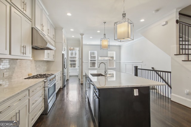 kitchen featuring sink, an island with sink, appliances with stainless steel finishes, decorative light fixtures, and dark hardwood / wood-style flooring