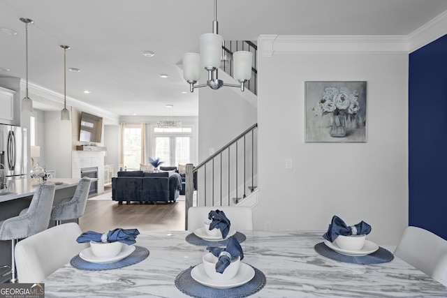 dining area with a tiled fireplace, crown molding, wood-type flooring, and a notable chandelier