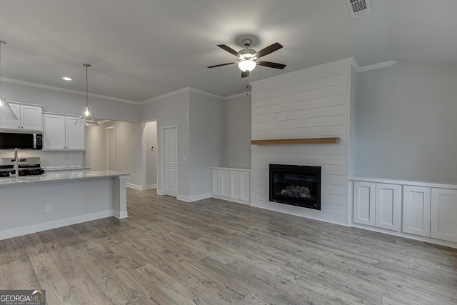 unfurnished living room with sink, a large fireplace, ornamental molding, ceiling fan, and light hardwood / wood-style flooring