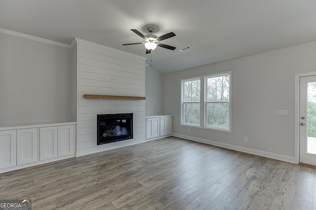 unfurnished living room with vaulted ceiling, a large fireplace, ornamental molding, ceiling fan, and light hardwood / wood-style flooring