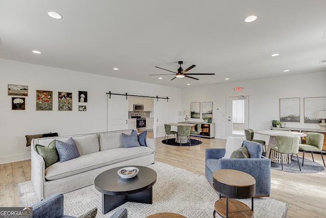 living room with a barn door, ceiling fan, and light wood-type flooring